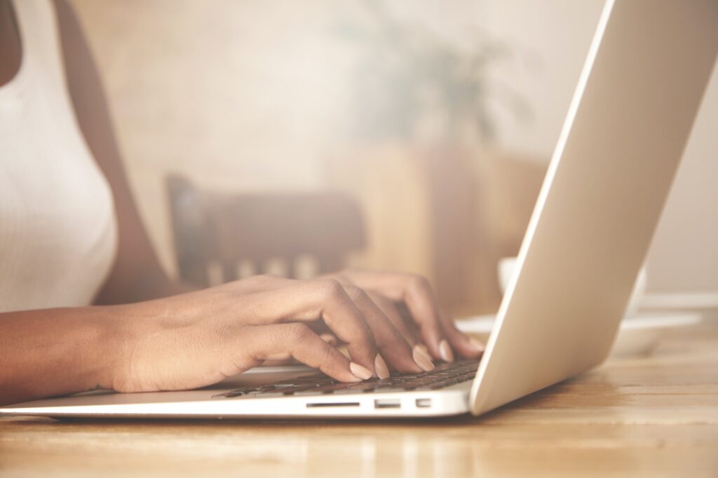Cropped portrait of African female blogger keyboarding on laptop computer, posting a new article on